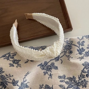 Detail of white pleated headband with pearl trim on an elegant floral tablecloth