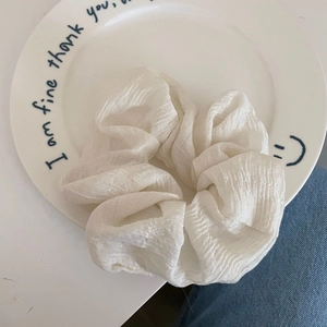 Detail view of white pleated fabric scrunchie with vertical texture on a white plate