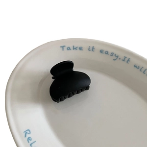 Matte black mini hair claw clip displayed on a white ceramic plate with blue printing