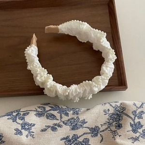 Elegant French style pleated white satin headband with delicate pearl trim on wooden tray