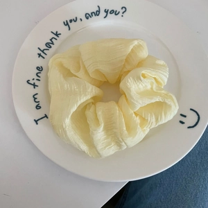 Close-up of light yellow pleated chiffon scrunchie placed on a decorative white plate