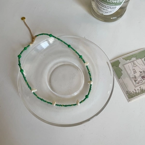 Détail du collier de perles vert menthe avec perles baroques sur plateau en verre
