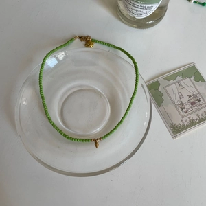 Détail d'un collier ras du cou perlé vert menthe sur plateau en verre avec fermoir doré