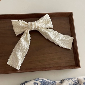 Detail of cream fabric bow hair clip with textured floral pattern and pearl trim edges