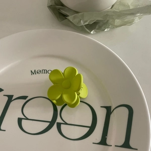 Détail d'une pince à cheveux fleur vert citron mat sur un plateau en céramique blanche