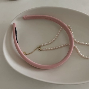 Serre-tête rose avec étiquette et collier de perles blanches dans un plat en céramique