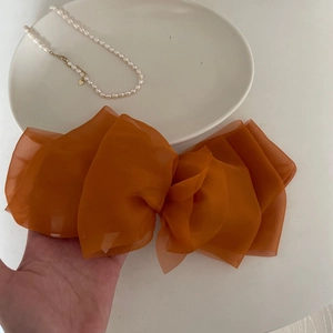 Elegant large deep orange mesh bow hair clip held by hand with pearl necklace decor