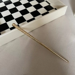 Detail showing the hammered texture and golden metallic finish of the sleek hair pin