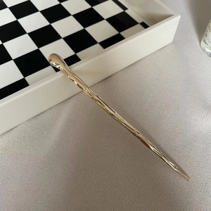 Detail of minimalist gold hair stick featuring a modern irregular molten metal texture