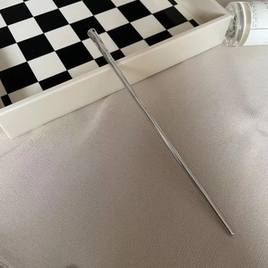 Minimalist silver metal hair pin with sleek glossy finish on beige fabric background