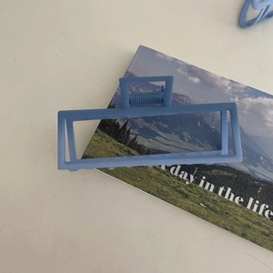 Matte light blue rectangular hair claw clip placed on a lifestyle magazine backdrop