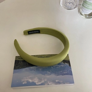Detailed view of green padded sponge headband with handmade label on white desk