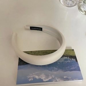 Handmade white padded satin headband with high crown effect on a white minimalist desk