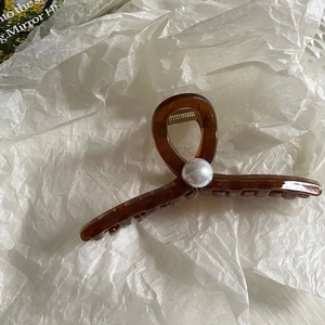 Detail of amber brown hair claw clip with large pearl on textured white background