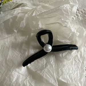 Close-up of black glossy hair claw clip with white pearl detail on white paper