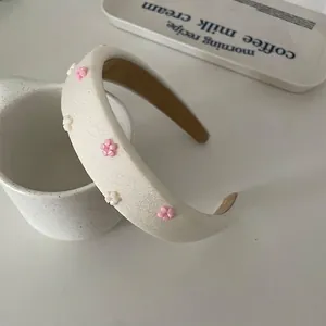 Elegant beige sponge headband with delicate pink floral accents leaning on ceramic decor
