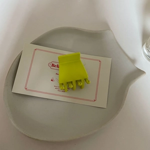 Gros plan d'une petite pince à cheveux vert mat sur un plateau décoratif en céramique blanche