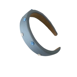 Light blue fabric headband with 3D floral decorations shown on a plain white background