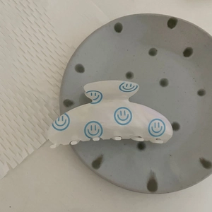 Large white hair claw clip with blue smiley flower patterns on a grey ceramic plate