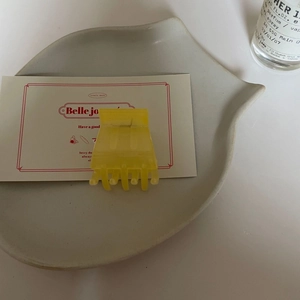 Détail d'une pince à cheveux jaune vif translucide en acrylique sur un plat en céramique