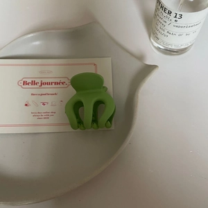 Détail d'une pince à cheveux mate verte posée sur un plateau décoratif en céramique blanche