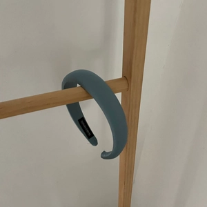 Puffy light blue satin headband with handmade label on a wooden stand display