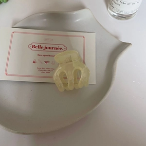 Gros plan d'une petite pince à cheveux en résine jaune crème sur une assiette en céramique