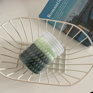Détail d'élastiques spirales dégradés verts dans un récipient en plastique clair
