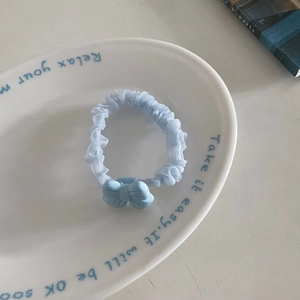Dettaglio di elastico in tulle azzurro con ciondolo a fiocco opaco su piatto
