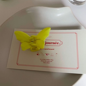 Détail d'une pince à cheveux papillon jaune mat avec ressort sur carte décorative