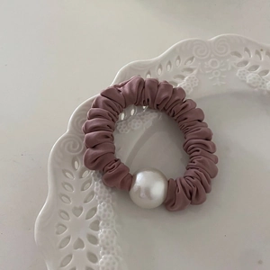 Chouchou élégant en satin rose avec une grande perle blanche sur une assiette en céramique