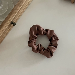 Gros plan d'un chouchou en satin marron élégant avec texture plissée brillante sur fond blanc