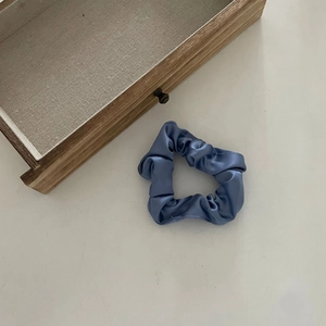 Détail de chouchou en satin bleu brumeux sur un fond blanc au style minimaliste