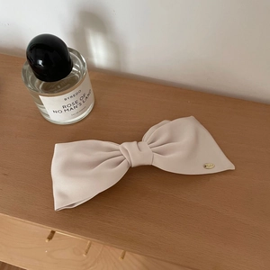 French style creamy beige satin bow hair clip with gold logo detail on wooden surface