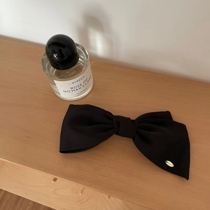 Detailed close-up of a smooth black satin bow hair clip with a golden metal logo plaque