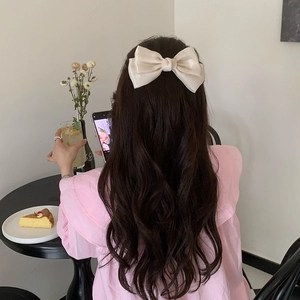Detail of a large cream satin bow hair clip on long wavy hair for an elegant look