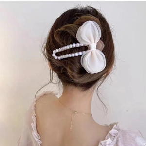 Détail d'une pince à cheveux élégante avec perles et nœud en gaze blanche sur un chignon