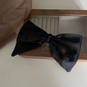 Elegant large black satin bow hair clip placed on a vintage wooden jewelry box