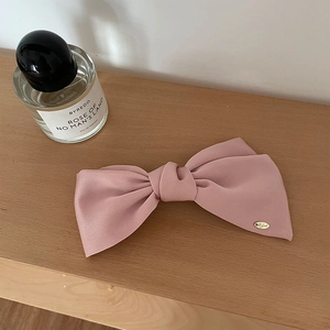 Pink satin bow hair clip with gold logo detail on a wooden table with perfume bottle