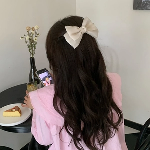 Detail of a large cream satin bow hair clip styled on elegant dark wavy hair