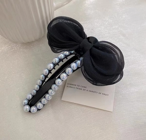Vue détaillée d'une grande pince à cheveux noire avec nœud en maille et perles