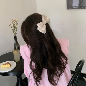 Elegant cream satin bow hair clip styled on dark hair in a cozy afternoon tea setting