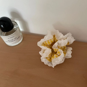 Nahaufnahme von gelbem Gingham-Spitzen-Scrunchie mit feiner Stickerei auf Holztisch