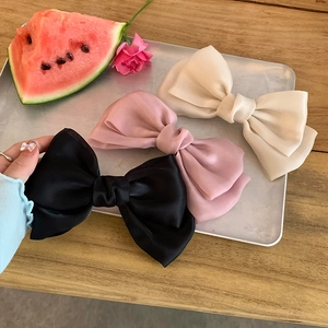 Three-piece satin bow hair clips in black, pink, and cream white on a silver tray