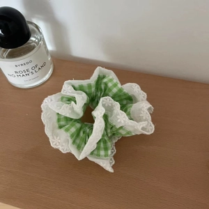 Grün-weiß karierter Spitzen-Scrunchie auf einer Holzoberfläche für das Haarstyling