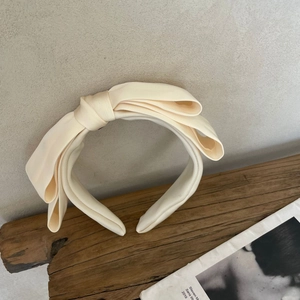 Elegant cream wide bow headband made of satin fabric displayed on a rustic wooden beam