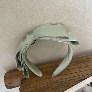 Detail of light green satin wide headband with oversized multi-layer bow for women