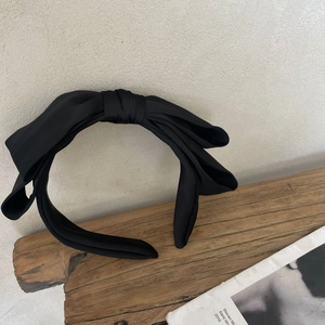 Detail of elegant black satin oversized bow headband on a natural wooden block