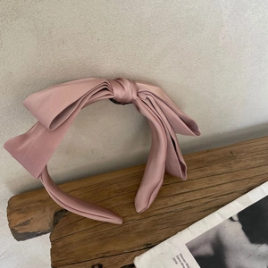 Detail of a large pale pink satin bow headband resting on a textured wooden block