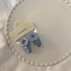Set of two light blue matte resin flower hair clips on a ceramic tray with white packaging